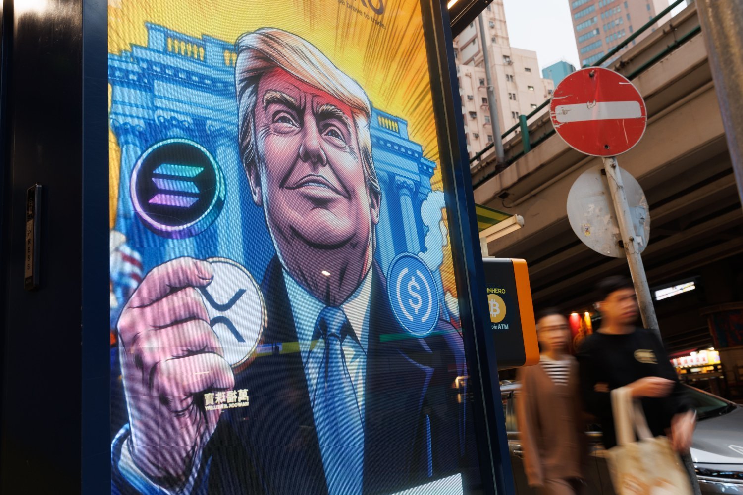 People walk past an advertisement feature Donald Trump with Solana, XRP, USDC Bitcoin