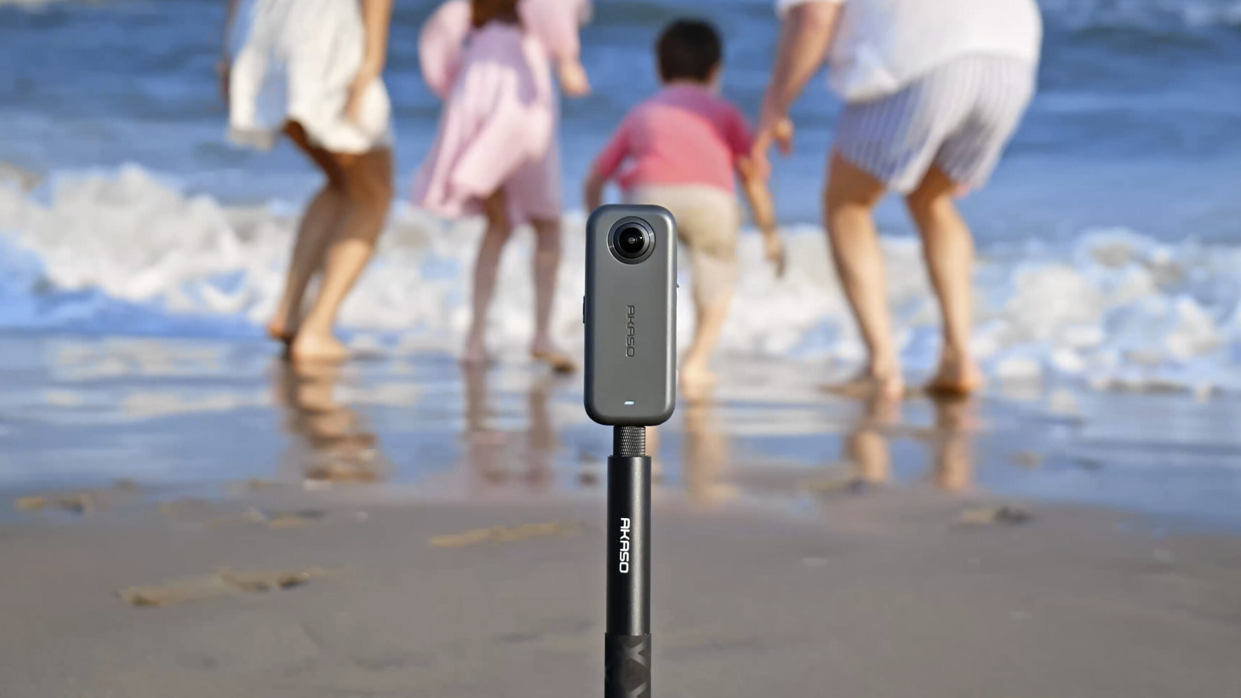 Akaso 360 camera attached to a selfie stick, filming a family on a beach